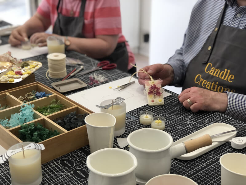 People wearing aprons sit at a table at a candle making class